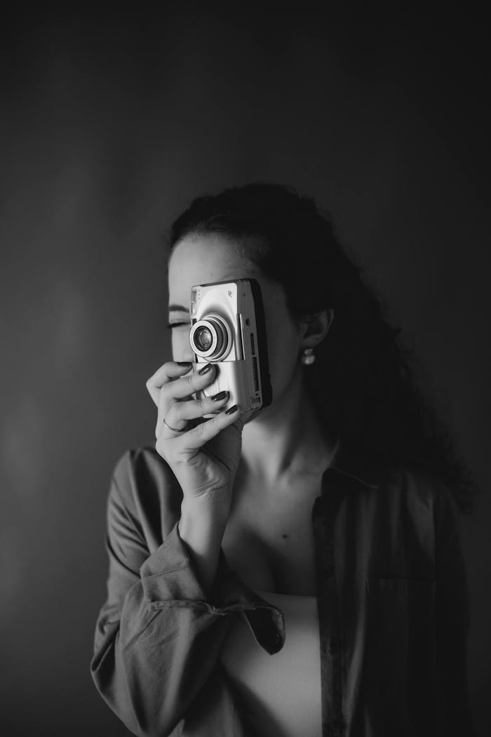 Black and white portrait of a woman holding a vintage camera in front of her face.